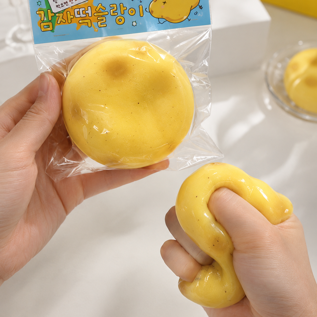 A person holds a packaged yellow squishy toy in one hand and squeezes another in the other hand. The product is shown both sealed in clear plastic with a blue cartoon header card and unpackaged, on a bright white tabletop with a blurred yellow bag in the background.